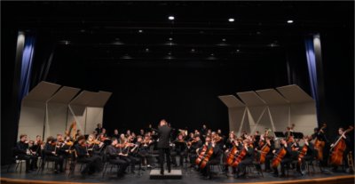concert band on stage with conductor in center, all musicians in black