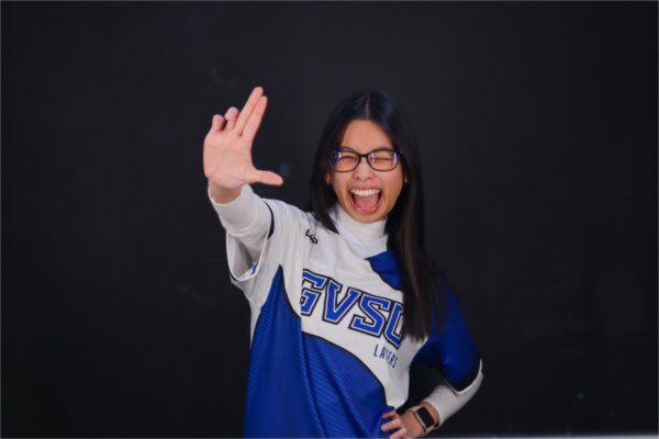 Sydney Lim in an esports jersey holding up the Laker L and smiling, she has glasses on