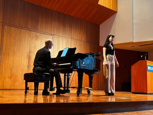 Vocalist singing on stage while accompanied by piano