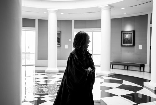 Black and white photo of Kyra walking through a circular atrium and looking back over her shoulder while laughing and crossing her arms.