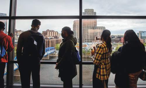 Students look out the window in the Eberhard center at the Grand River and Downtown Grand Rapids