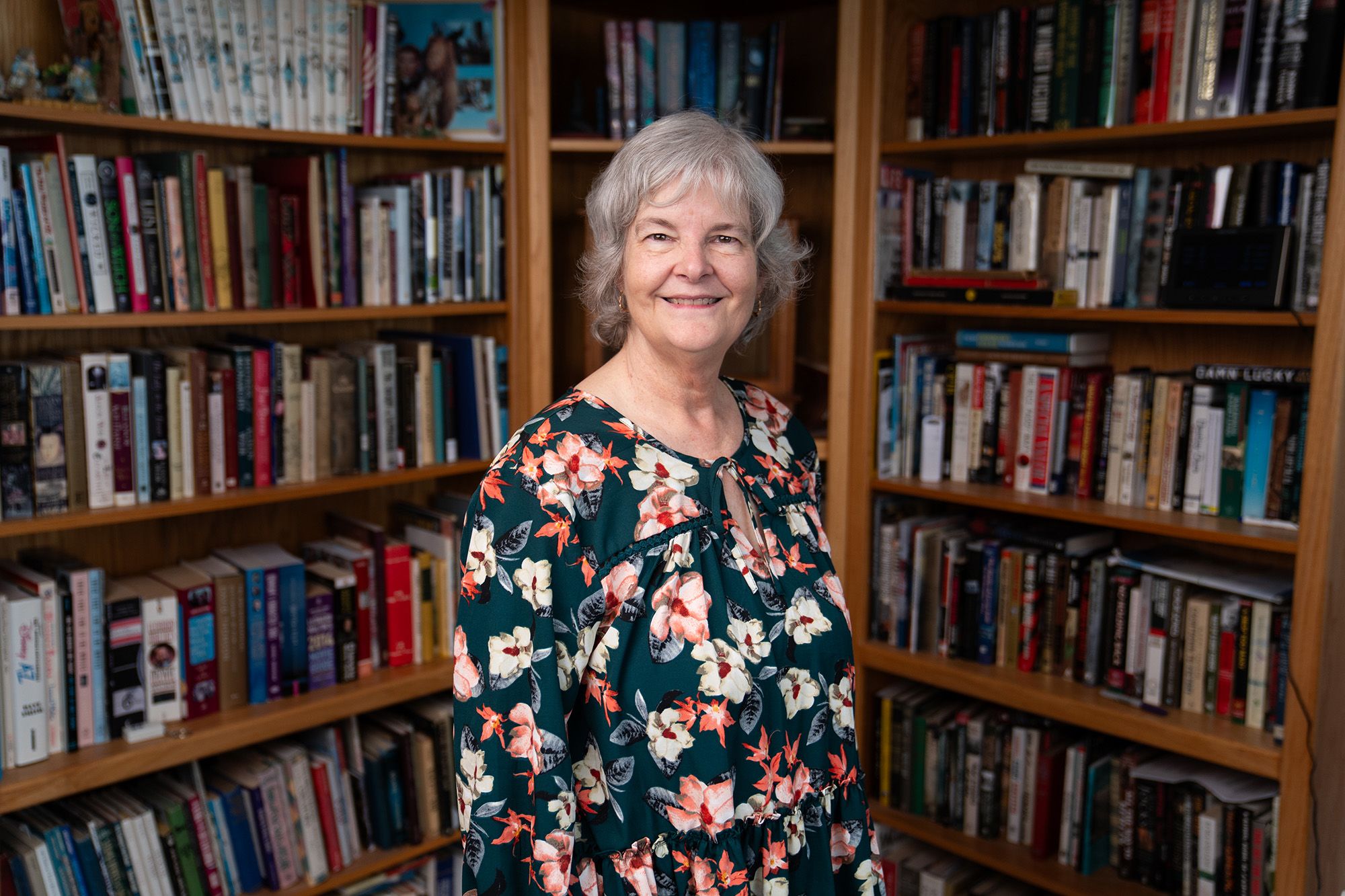 Alison McManus Walters stands in front of bookcases in a floral print shirt