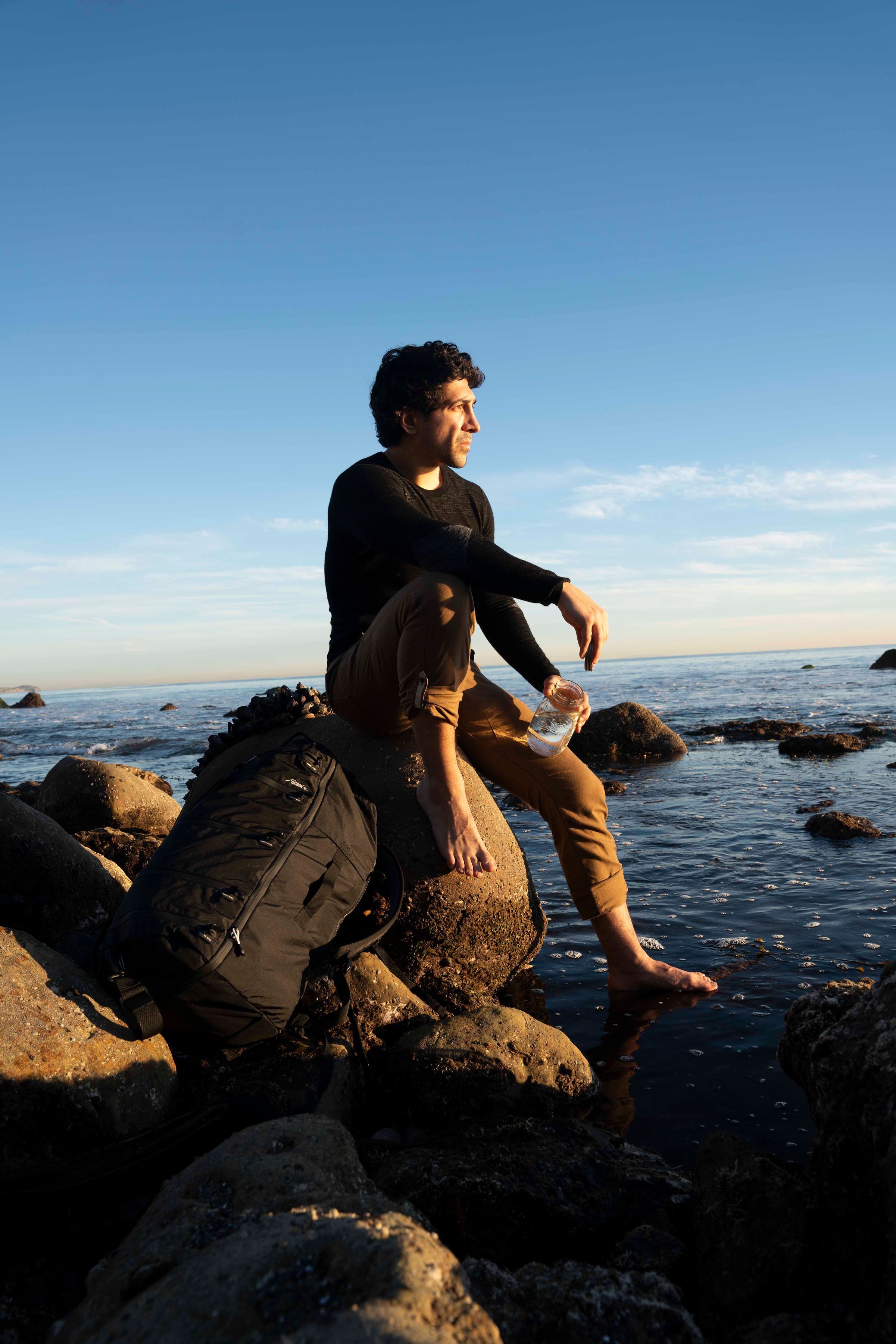 Michael Zervos sitting on a rock in the Pacific Ocean, coastline