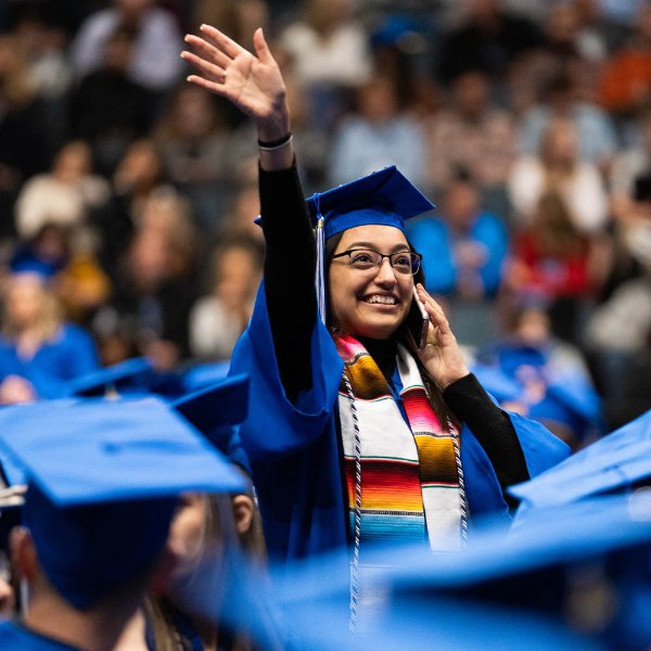 A graduating student stands and waves to her family at a GVSU commencement ceremony.