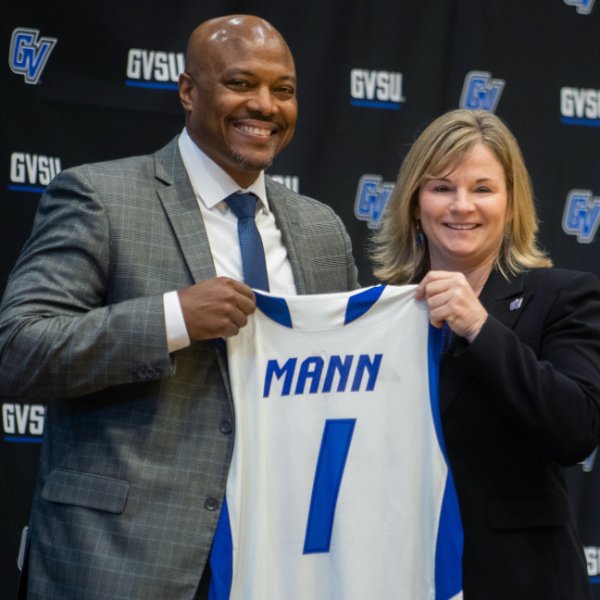 Men's basketball coach Cornell Mann and Director of Athletics Keri Becker hold up a jersey with Mann's name.