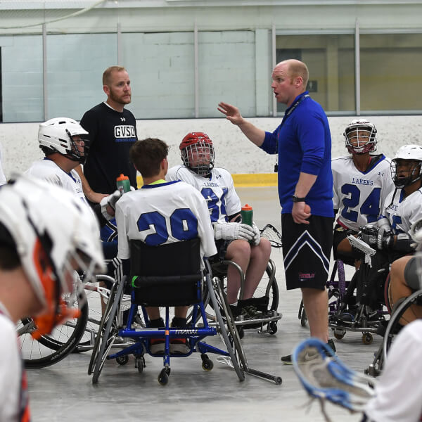 coach standing in center of wheelchair lacrosse athletes