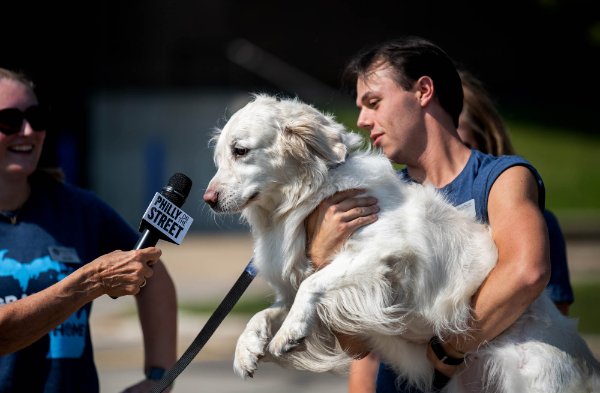 A college student holds a dog while it's being "interviewed" with a microphone.  