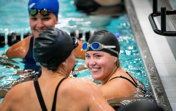  College students laugh together in a pool during a swimming class. 