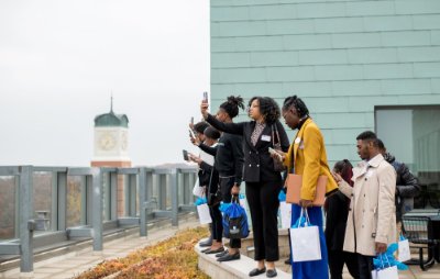 students stand on fourth floor balcony of Pew Library to take cell phone photos