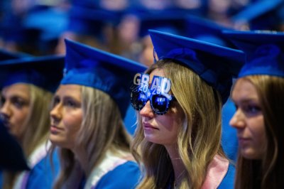 A grad sits at commencement while wearing sunglasses that say "Grad 2023" above the eyes. 