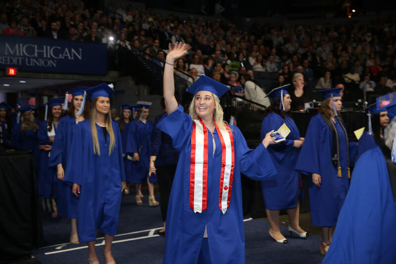 woman waving entering arena in graduation regalia