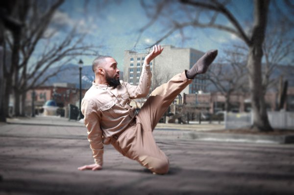 A dancer balances on one knee with a hand on the ground while extending the other leg and arm.