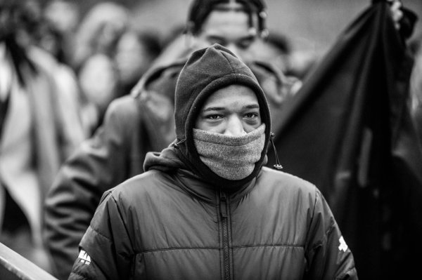 A person, bundled up in a coat and face covering, walks amongst others. 