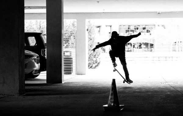 Silhouette of a person on a skate board jumping inside a parking garage under a building. 
