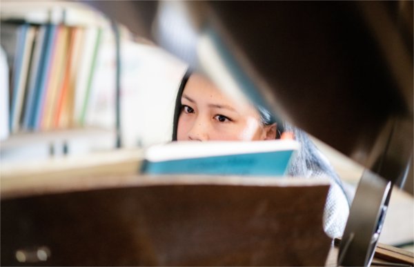 A person seen through the opened top of a baby grand piano peers at a music book.