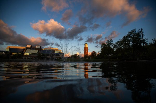 A carillon tower is reflected in water on a college campus.  