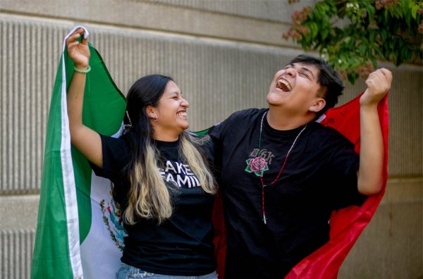  Two college students hold up the Mexico flag while laughing together. 