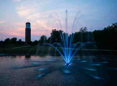 A blue fountain is seen near a carillon tower during sunset.