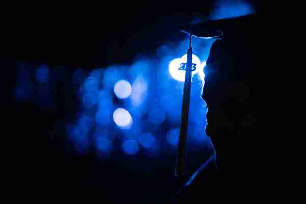 A person wearing a cap and gown is illuminated against blue lights. 