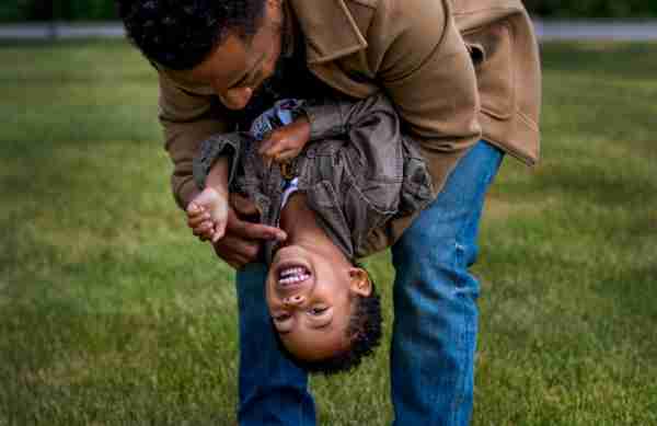 A man holds his son upside down as he laughs.  