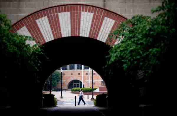 A person is framed by an arch of a college campus as they walk on the sidewalk.  