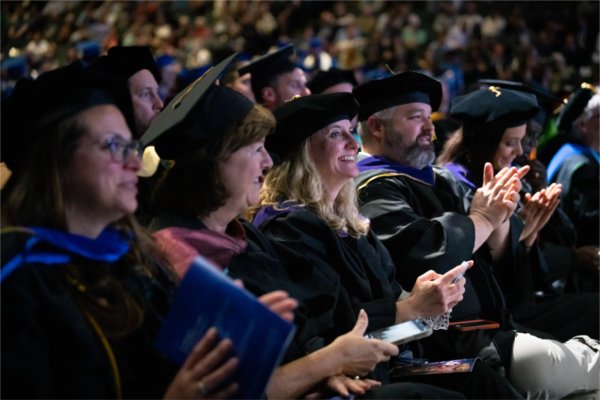 Faculty and Staff smile and clap in the audience during Commencement.