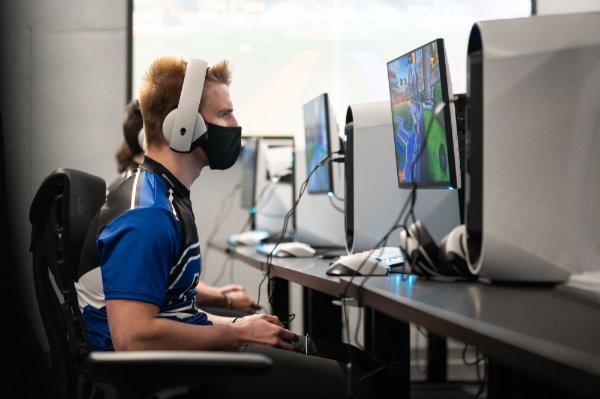 Esports club member sits in front of computer, wearing a mask and headphones