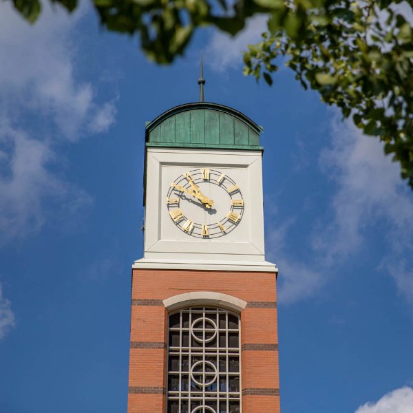 The top of a carillon with a clock is shown with tree branches in the foreground.