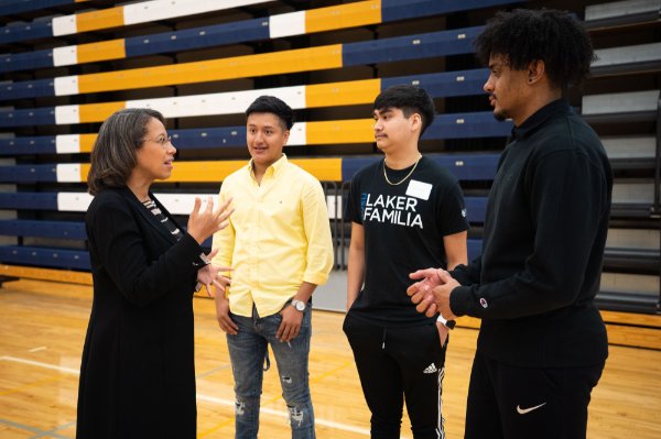 woman standing talking with three students, also standing in a gymnasium