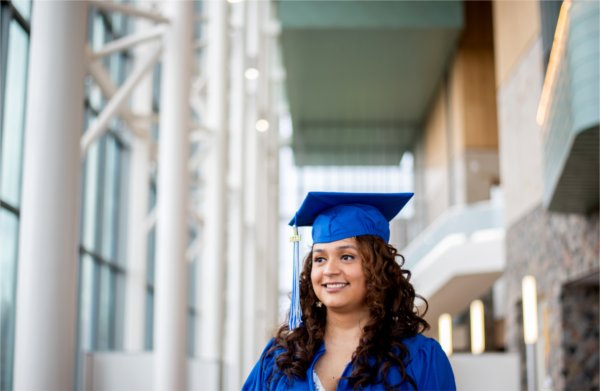 A person wearing a cap and gown smiles while looking off to the side. Tall white pillars are behind the person.