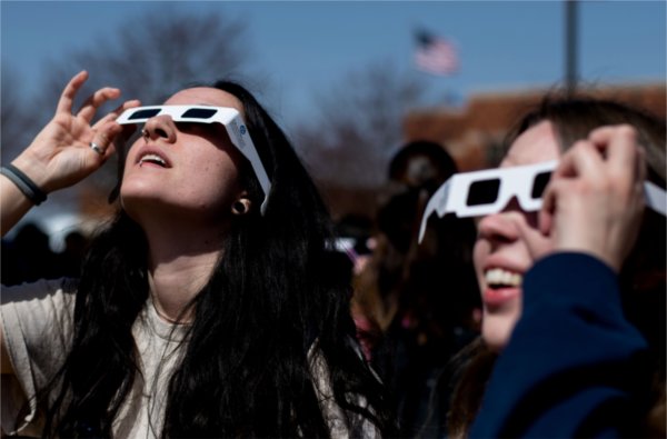 Two people wearing special glasses for a solar eclipse look upward.