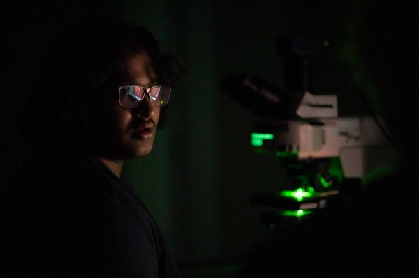 A person looks toward a microscope as a green glow reflects in their glasses
