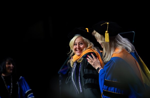 After a hooding ceremony, a graduate is congratulated.