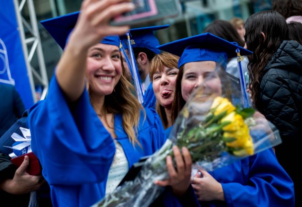  A person sticks out their tongue while posing for a photo with graduates.