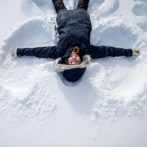 Student in winter coat and snow pants lies down and makes a snow angel.