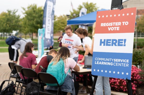 Students sit at a table outside on campus to register to vote through the Secretary of State Mobile unit.