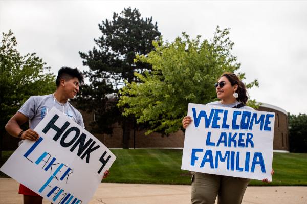 Two people holding signs that read "Honk 4 Laker Familia" and "Welcome Laker Familia"