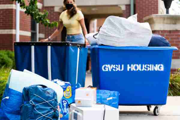 Two blue bins with the words "gvsu housing" written on them hold students belongings outside of a living center.
