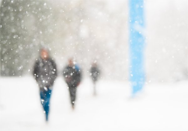  Large snowflakes fall as students walk through the snowy scene on a college campus. 