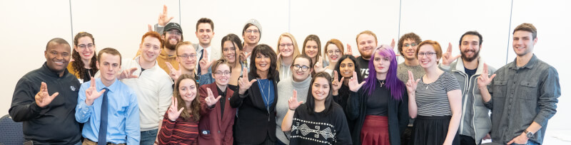 Philomena Mantella poses for a photo with a group of student senators. The group is smiling and holding up their index and middle fingers near their thumbs in the 'Laker Up' gesture.