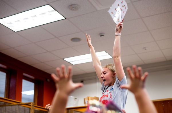 A master of public health student raises her hands in the air as part of a yoga exercise with elementary students.