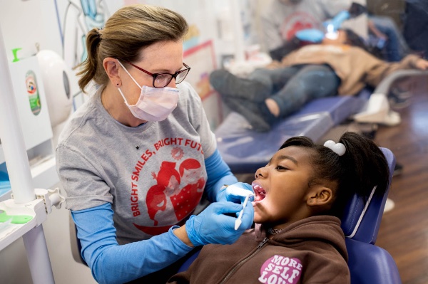 A dental hygienist performs a screening on a girl's teeth.