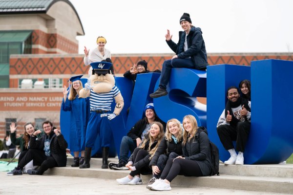 People and the Louie mascot sit and stand among the GVSU letters.