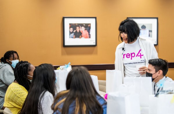 A person wearing a T-shirt that says "rep 4" stands while talking to people who are seated.