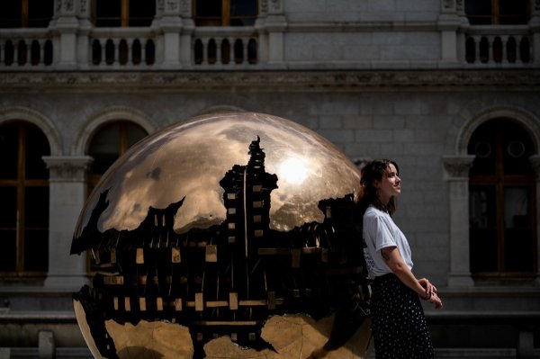A person leans against a metal sphere and looks into the distance.