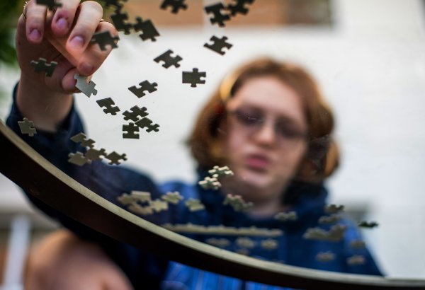  Looking through the bottom of a glass table up at a person's hand putting together a puzzle and their face in the background.