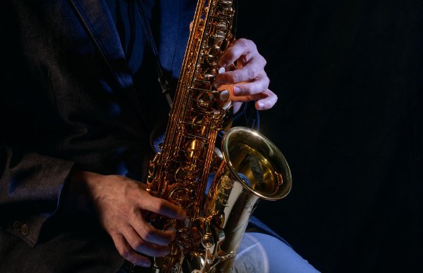 The bottom part of a saxophone is shown while a seated musician plays it.