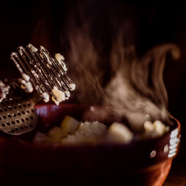 A bowl of potatoes with steam coming off of them, with a hand masher propped on the side
