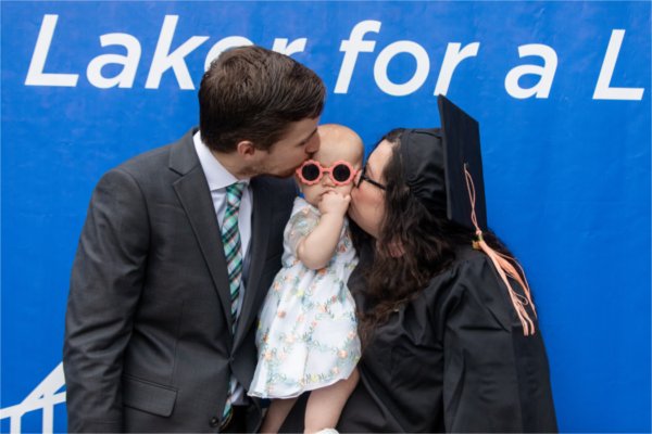  Two people, one wearing a cap and gown, kiss a baby wearing flower sunglasses.