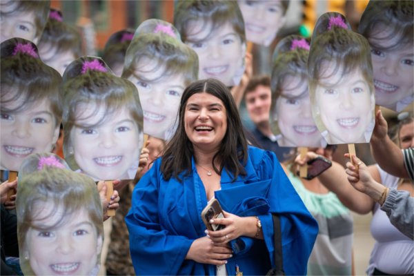  A graduate laughs as they are surrounded by cutout photos of themselves as a preschooler. 
